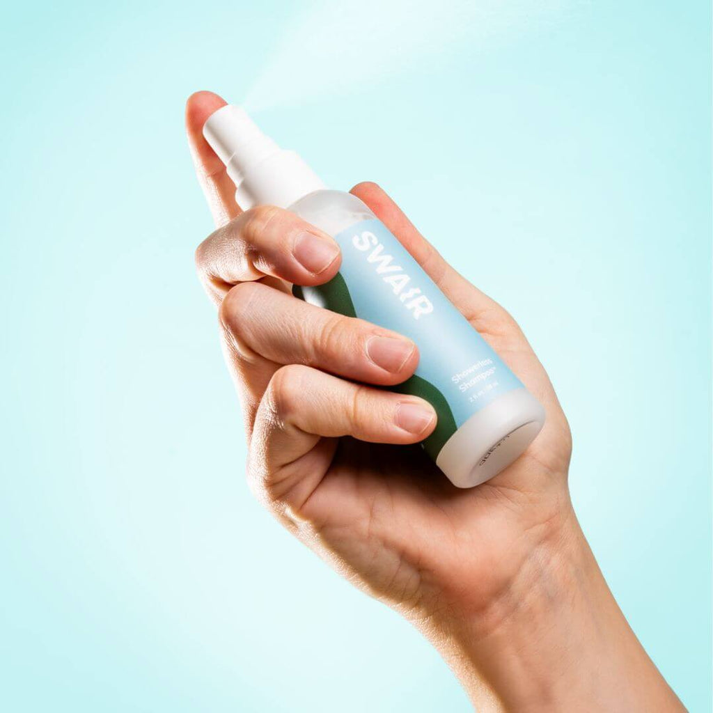 Mini SWAIR Showerless Shampoo bottle being held in a hand on a blue background